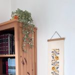 הדפסה ייחודית על בד קנבס בין מוטות עץ כפריים לתלייה על קיר באווירה כפרית וטבעית בפורמט צר ואורך מתאים לתליה על קיר צר במעברים עיצוב מיוחד עם המילים מזמור שיר חנוכת הבית מתנה לחנוכת בית סגנון דמוי רקמה חום חרדל