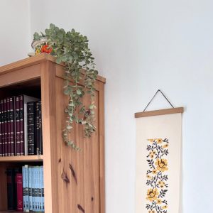 הדפסה ייחודית על בד קנבס בין מוטות עץ כפריים לתלייה על קיר באווירה כפרית וטבעית בפורמט צר ואורך מתאים לתליה על קיר צר במעברים עיצוב מיוחד עם המילים מזמור שיר חנוכת הבית מתנה לחנוכת בית סגנון דמוי רקמה חום חרדל