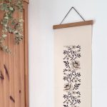 הדפסה ייחודית על בד קנבס בין מוטות עץ כפריים לתלייה על קיר באווירה כפרית וטבעית בפורמט צר ואורך מתאים לתליה על קיר צר במעברים עיצוב מיוחד עם המילים אך טוב וחסד מתנה לחנוכת בית סגנון דמוי רקמה חום מוקה