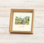 מסגרת תמונה ייחודית ריבוע עומד עם עובי להנחה על מדף עם פרינט של איור כמו צבעי מים עדין של נוף מאיר ושליו גווני ירוק שמנת תכלת בהיר עם רכב נוסע בשביל כפרי עם הכיתוב לאסוף רגעים