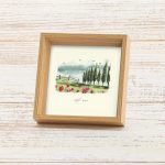 מסגרת תמונה ייחודית ריבוע עומד עם עובי להנחה על מדף עם פרינט של איור כמו צבעי מים עדין של נוף מאיר ושליו גווני ירוק ברושים פרחים ורודים שמנת בהיר תכלת עם הכיתוב רסיסי אושר